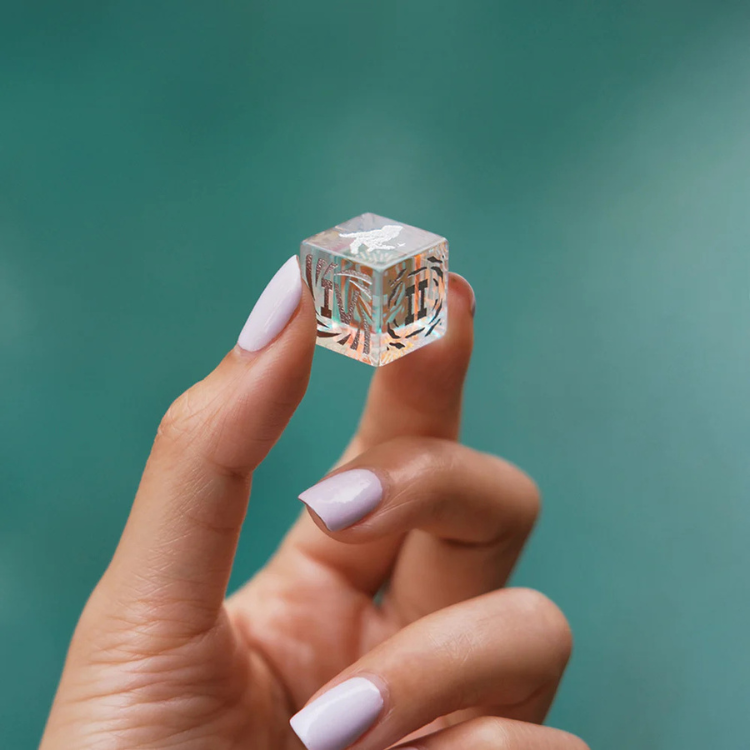 Hand holding a clear acrylic cube game piece with etched designs, House of Vices wellness store
