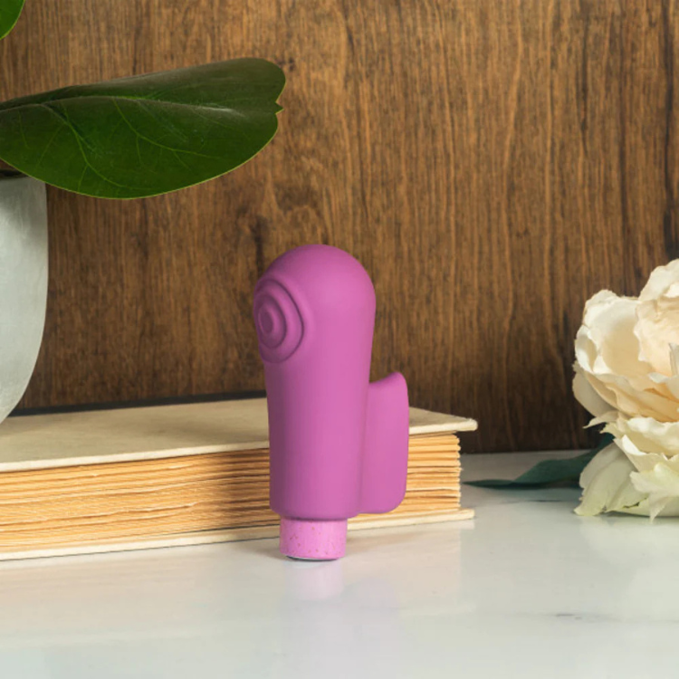 Purple silicone bullet vibrator and sleeve on a table near a plant and white flower