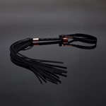 Black leather whip with gold accents on reflective surface, House of Vices adult wellness product