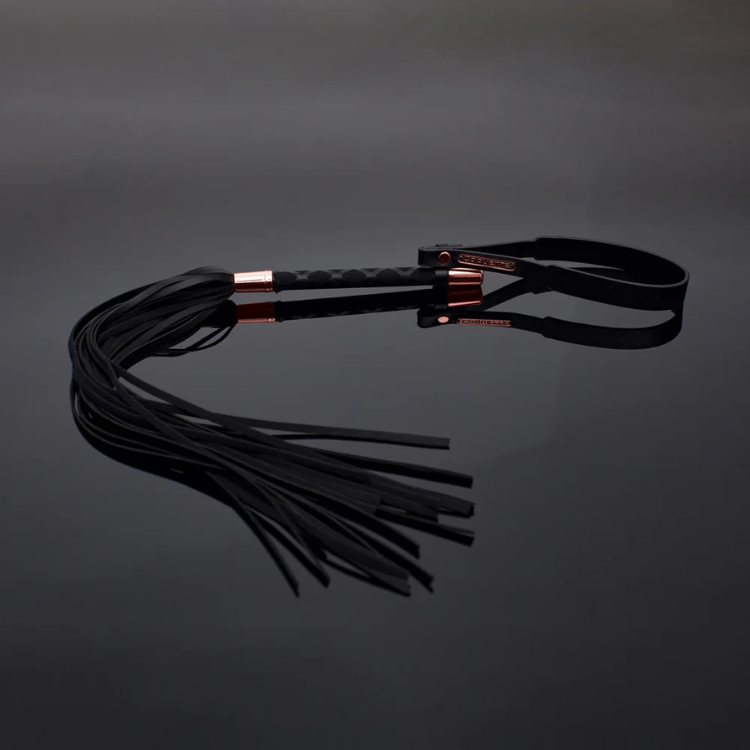Black leather whip with gold accents on reflective surface, House of Vices adult wellness product