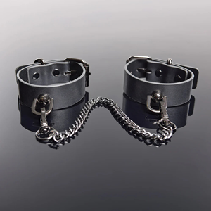 Grey faux leather pleasure cuffs with silver chain on reflective surface, House of Vices wellness essentials