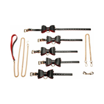 Black and red leather bow bondage set with gold chains, cuffs, collar, and leash
