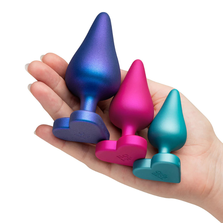 Hand holding three colorful heart-base silicone wellness plugs from House of Vices