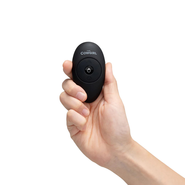 Hand holding a black remote control for The Cowgirl Saddle Machine