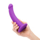 A hand holding a purple silicone dildo toy against a white background.