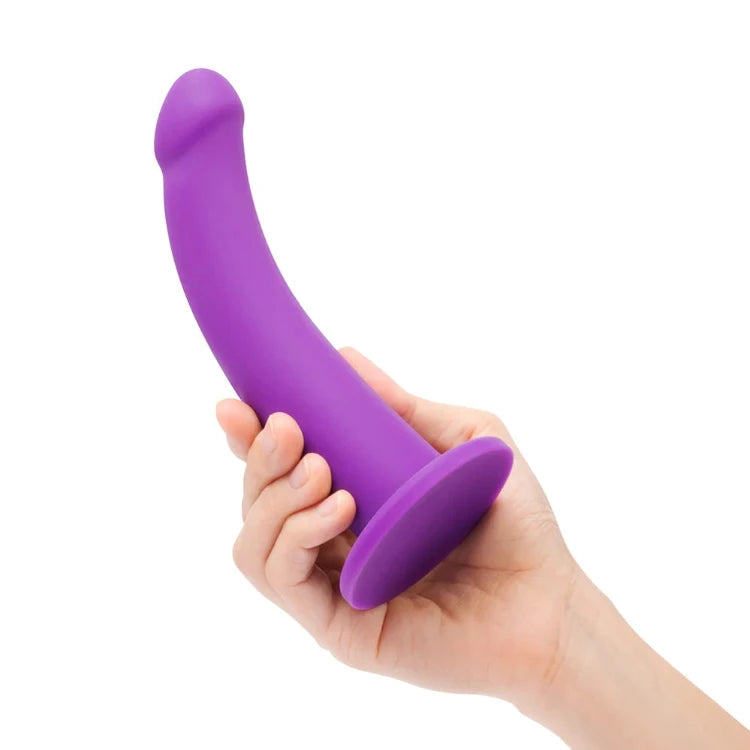 A hand holding a purple silicone dildo toy against a white background.