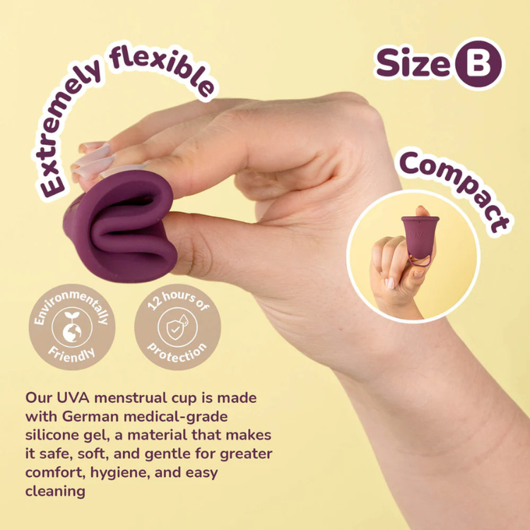 Hand holding a folded, flexible size B purple menstrual cup made of medical-grade silicone.